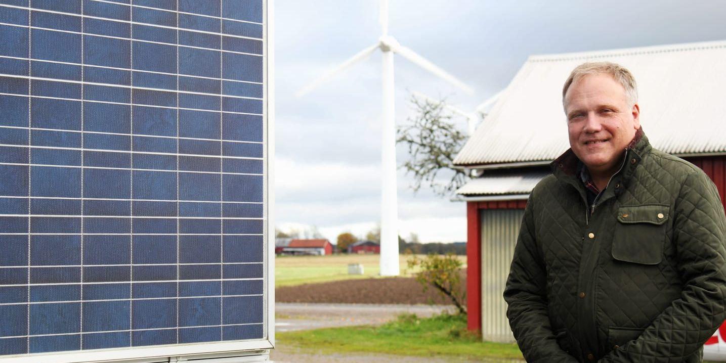 På ladugårdsväggen har Magnus Johansson installerat solcellspaneler och i bakgrunden syns två vindkraftverk på hans åker.