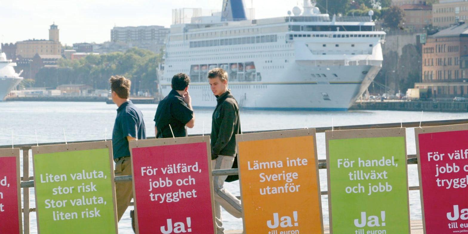Jorå. För nästan tjugo år sedan röstade svenska folket nej till euro, det är hög tid att omvärdera det beslutet.
Människor promenerar på Skeppsbron och passerar valffischer med budskapet JA inför folkomröstningen om euron den 14 september 2003.