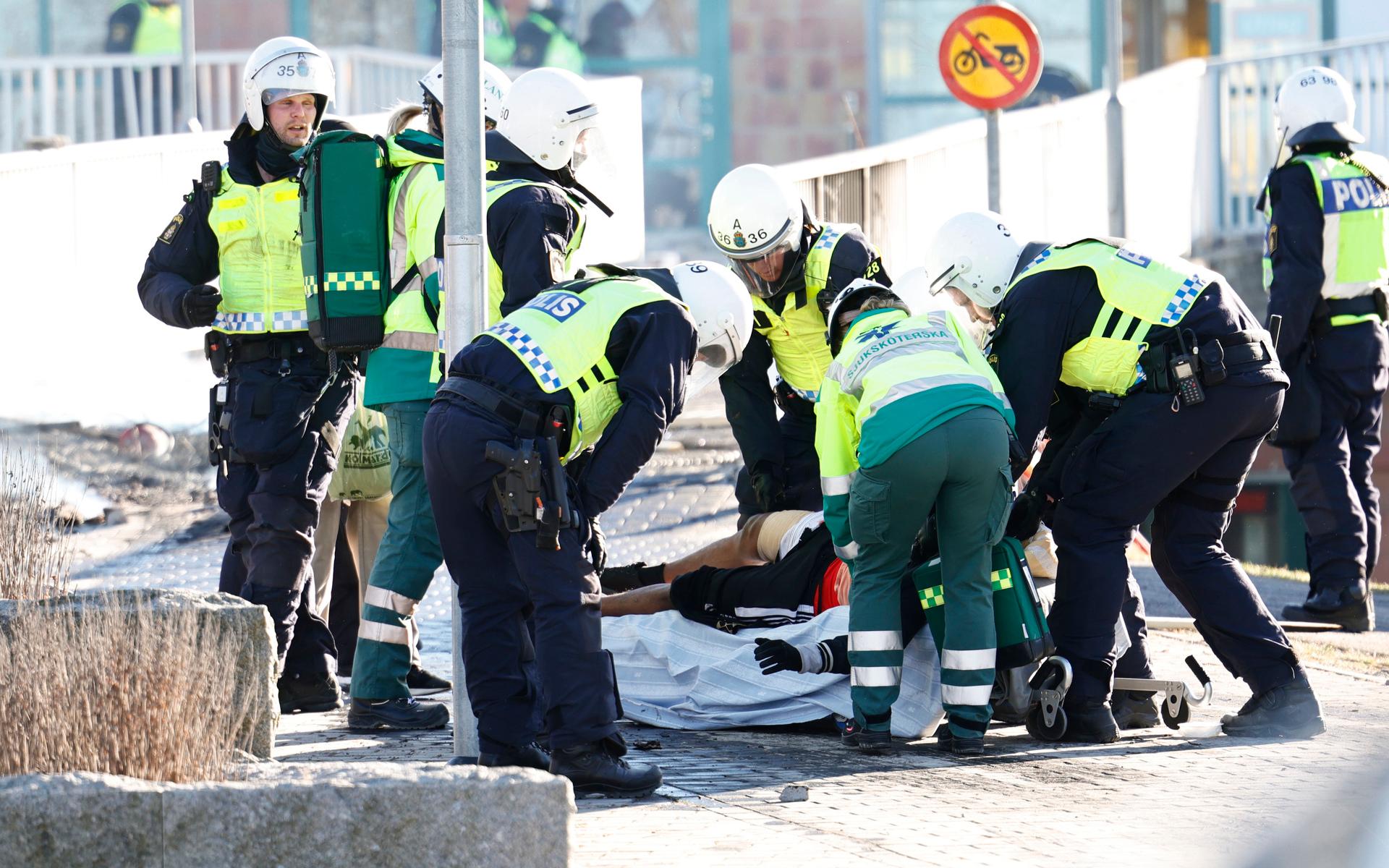 Polis och ambulanspersonal lägger en skadad man som skjutits i benet på en bår under upploppen i Navestad i Norrköping på påskdagen.Oroligheterna utlöstes av att den högerextrema provokatören Rasmus Paludan har sagt att han ska återvända till Östergötland för nya demonstrationer under dagen.