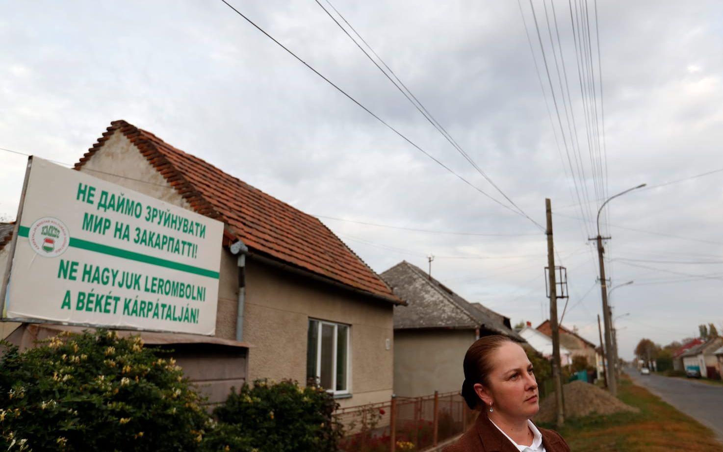 In this Thursday, Oct. 18, 2018, photograph Livia Balogh, an official of the Transcarpathian Hungarian Cultural Association, stands in front of a billboard saying "Let's not allow peace to be destroyed in Transcarpathia!" in Chop, Ukraine. A new education law that could practically eliminate the use of Hungarian and other minority languages in schools after the 4th grade is just one of several issues threatening this community of 120,000 people. Many are worried that even as Ukraine strives to bring its laws and practices closer to European Union standards, its policies for minorities seem to be heading in a far more restrictive direction. (AP Photo/Laszlo Balogh)