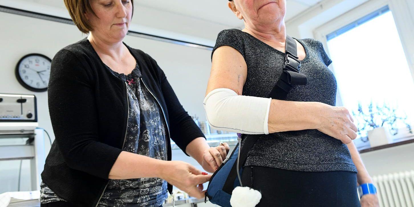 Inger Axelsson hjälper patienten Lilian Svensson med den portabla pumpen för cytostatika. Med den är det möjligt att röra sig fritt under pågående behandling.