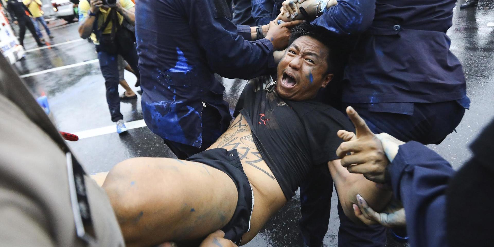 Thailändsk polis frihetsberövar en demokratiaktivist som hällt blå färg på gatan i Bangkok.
