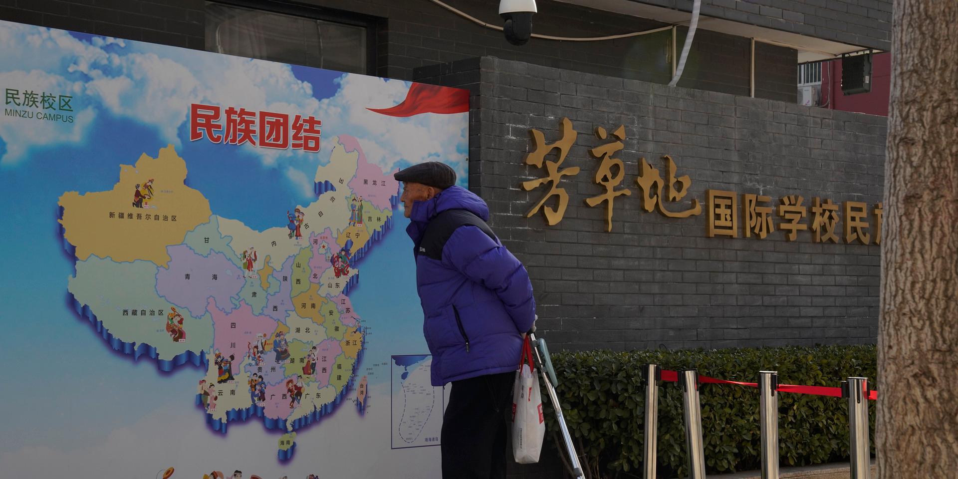 En äldre man i Peking tittar på en karta över Kina, där regionen Xinjiang syns uppe i det vänstra hörnet. På bilden står texten 'etnisk enighet'. Arkivbild.