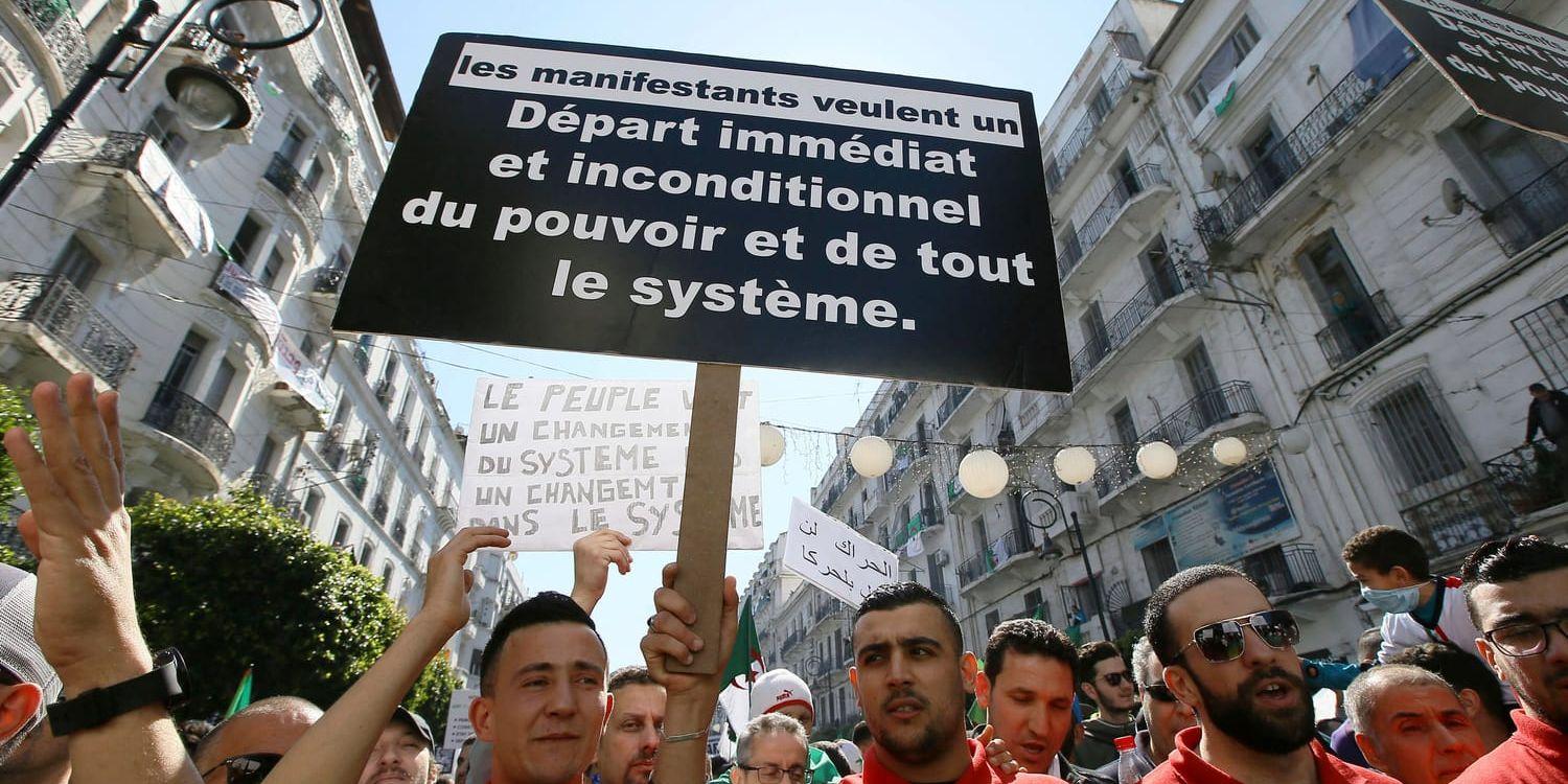 En demonstrant håller upp ett plakat som kräver systemskifte i Algeriet.